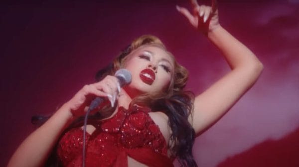 Kali Uchis in all red clothing, nail color, and red lips. She is dancing and singing with a microphone for 2021 music video for her song "telepatia"
